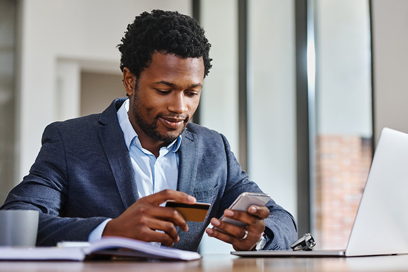 Man smiling in a suit reading his credit card number and entering it into his phone