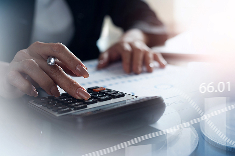 Close-up of a person using a calculator with documents and charts in the background.